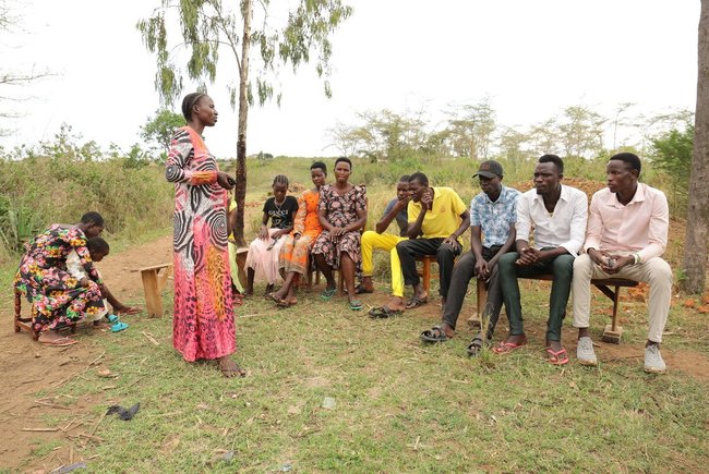 A woman speaks to a group of people sitting in a circle, outdoors